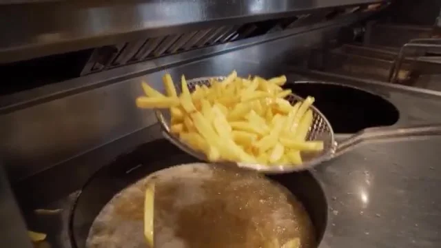 A metal skimmer lifts fries from a fryer